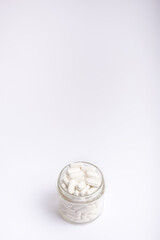 White tablets in glass transparent jar on white background. 