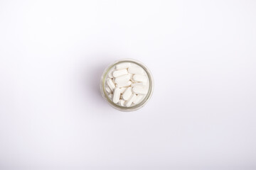 White tablets in glass transparent jar on white background. 