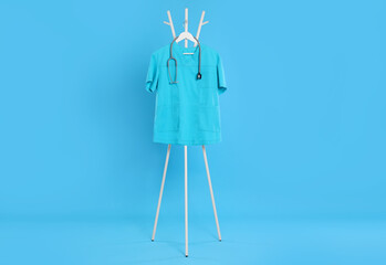 Turquoise medical uniform and stethoscope hanging on rack against light blue background