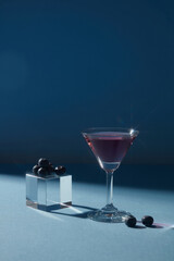 Transparent cube with blueberries placed on, decorated with a cocktail glass of purple liquid over a dark background. Promoting product extracted from Blueberry (Vaccinium Corymbosum)