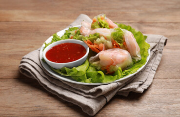 Tasty spring rolls served with lettuce and sauce on wooden table