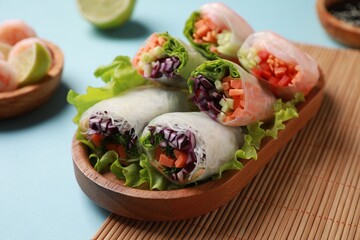 Tasty spring rolls served with lettuce on light blue background, closeup