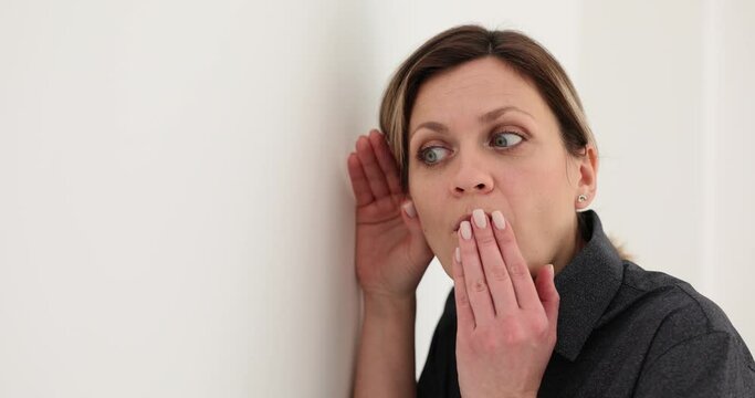 Curious woman listens to discussion of colleagues in office. Attentive woman with surprised expression puts ear to wall