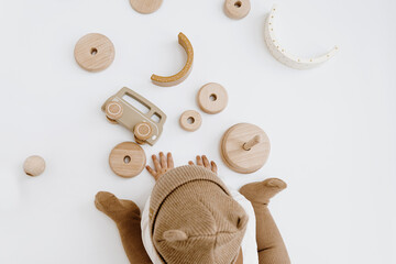 Top view of cute one year old baby in brown hat plays with stylish wooden toys. Minimal baby fashion online shop, online store concept