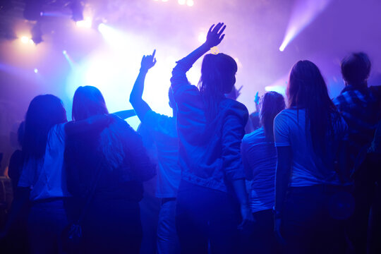 Purple, neon light and people dancing at music festival from back, night and energy at live concert event. Dance, fun and group of excited fans in arena at rock band performance or crowd at party.