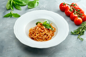 Italian spaghetti pasta with tomatoes and shrimps in a white plate on a gray background