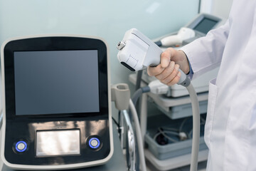 Closeup of young cosmetologist using modern laser machine in beauty clinic