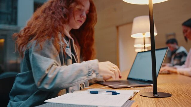 Young teenage girl doing research for an assignment in a library, using a laptop to access scholarly articles online. Female college student working hard towards acquiring a university degree.