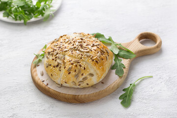 Baked in puff pastry cheese sprinkled with seeds decorated with fresh arugula leaves on a wooden board on a gray textured background