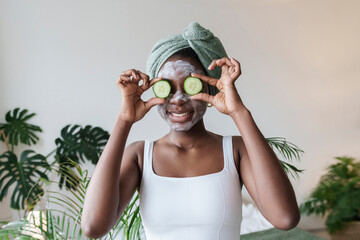 Smiling woman holding cucumber over eyes at home