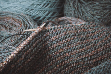 Skeins of wool yarn, wooden knitting needles, an unfinished scarf in the process of knitting.