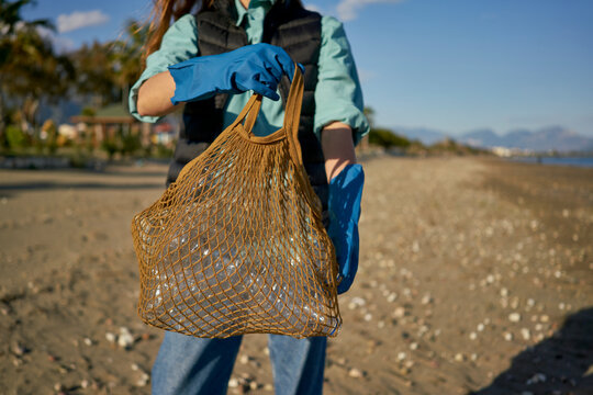 Volunteer holding mesh bag with plastic bottles at beach