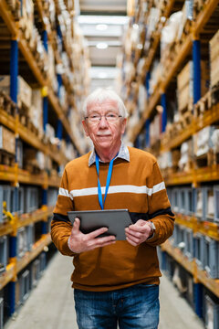 Confident senior man standing with tablet PC in warehouse