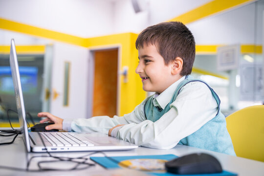 Smiling boy using laptop sitting at desk in school