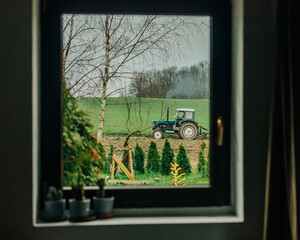 Farmer ploughing with tractor in field seen through window