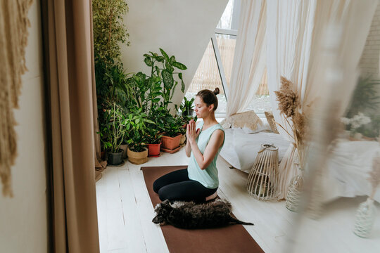 Woman meditating with hands clasped by Schnauzer dog at home