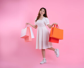 Fototapeta premium full body image of asian woman holding shopping bag and posing on pink background