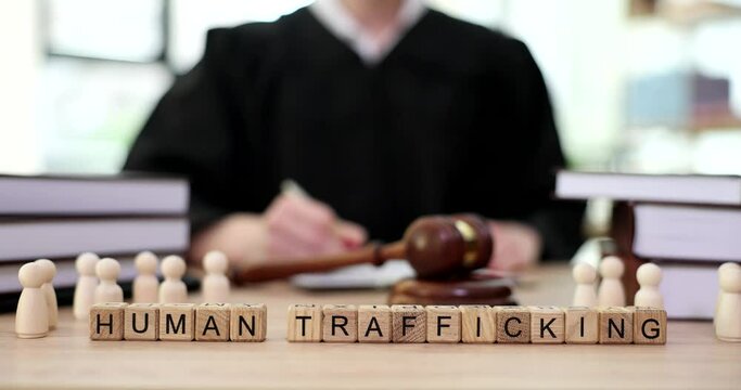 Word human trafficking and wooden men on table of judge with gavel in courtroom closeup 4k movie slow motion. Human trafficking and sexual slavery criminal liability concept 