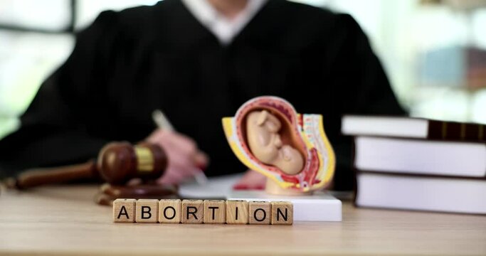 Model of fetus in uterus and word abortion on judge table closeup 4k movie slow motion. Official ban on abortion concept 