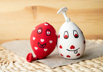 Two funny homemade sensory stress balls, made of balloons and filled with flour. Red and white balls with hearts and funny drawn faces, wood background. - obrazy, fototapety, plakaty