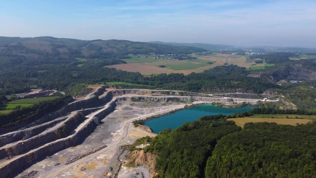 Aerial view discovering a large open-pit mine with an industrial lake and surrounding nature