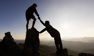 Silhouette of Two male  hikers climbing up mountain cliff and one of them giving helping hand....