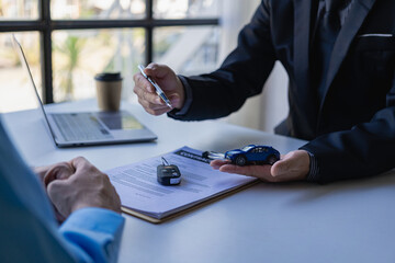 Salespeople introduce customers sitting at tables with small cars and car concept keys, car dealership sales, and new owners have entered into contracts to sell and rent cars with insurance.