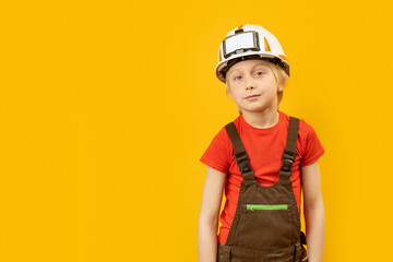 Studio portrait of blond teenage boy in white helmet and work overalls on yellow background. Copy space.