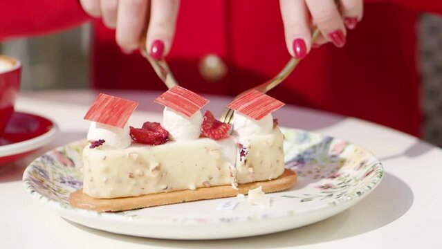 Close up female hands with knife and fork cutting cake and drinking coffee in cafe. Woman in red clothes eating dessert