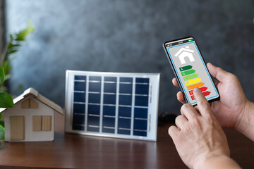 Smart home display and model house with solar panel, energy efficient technology concept. Energy efficiency mobile app on screen rating with arrows and house.