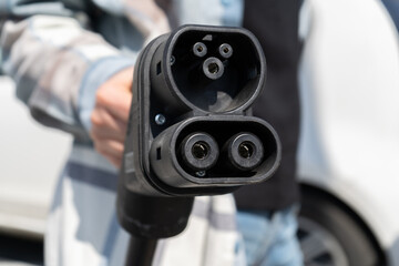 Woman holding CCS fast charging socket type 2. Combined Charging System Combo 2 connector plug for electric vehicles at EV car charging station. Female hand plugging in charger into electric car.