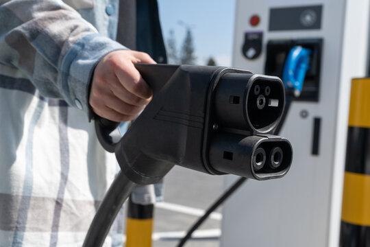 Woman holding CCS fast charging socket type 2. Combined Charging System Combo 2 connector plug for electric vehicles at EV car charging station. Female hand plugging in charger into electric car.