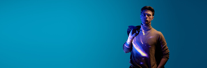 Handsome, serious, young guy with digital kosmos reflection on clothes and body posing against blue background in neon light. Concept of modern photography, art, cyberpunk, techno, creativity. Banner © master1305
