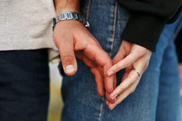 Close up couple hands touching on field over beautiful sunset. Casual clothes. Man hands wear watch, woman hand ring .