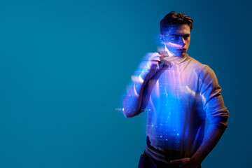 Handsome, stylish, young man with serious expression posing with digital kosmos reflection on body and clothes against blue background in neon. Modern photography, art, cyberpunk, creativity concept © master1305