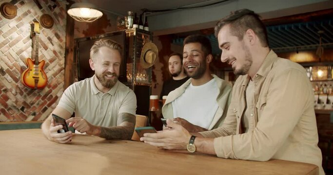 Looking at smartphones unconscious about the surroundings. Multiethnic group of people using their smartphones actively. Three men using their smartphones while sitting in pub after work.