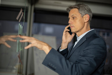 Portrait of businessman talking to the phone in office. Man writing ideas on colorful stickers on glass wall