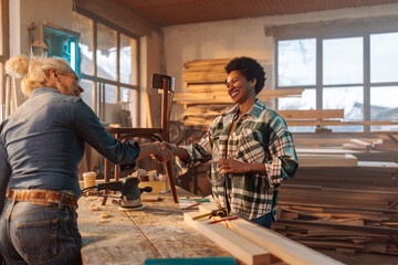 Female carpenters shaking hands in workshop.