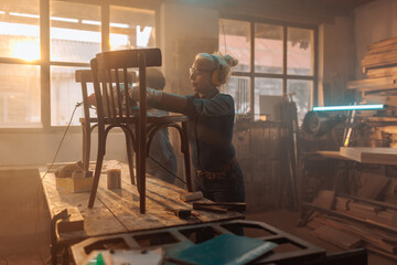 Female restaurateurs sanding furniture in workshop.