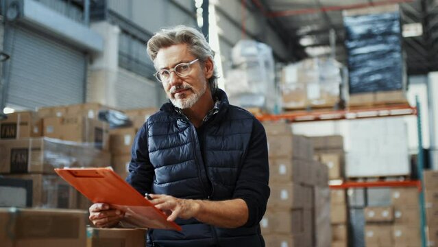 Mature and experienced warehouse manager smiles at the camera after reviewing inventory management records in a distribution center