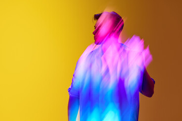 Young stylish man standing against gradient yellow background with mixed neon multicolored lights effect. Futurism. Concept of modern photography, art, cyberpunk, techno, creativity, beauty