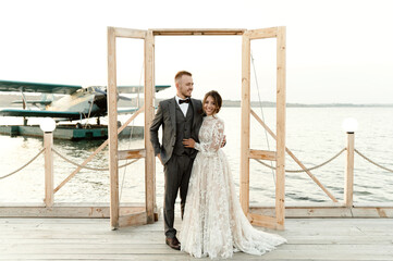 a wooden wedding arch overlooking the sea, a wedding couple stands against the background of a wooden arch and an airplane on the water