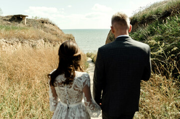 young bride and groom walk overlooking the sea. happy wedding day of the newlyweds. couple gently holding hands while in the wild