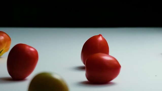 Reversed Slow Motion Shot of Tomatoes of Different Colours Falling, Bouncing and Rolling onto a White Surface untill they Stop Moving (HD)