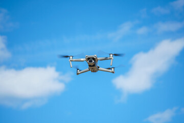 a drone with a high-resolution digital camera flies against a blue sky with clouds, a drone hovers in the air against the sky, a copter hovers in the air