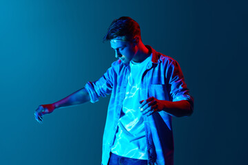 Young man standing with digital neon lights reflection on face and body over blue background....