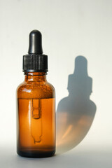 The amber glass dropper bottle with the serum inside casts a shadow. Vertical image, flat lay, copy space.