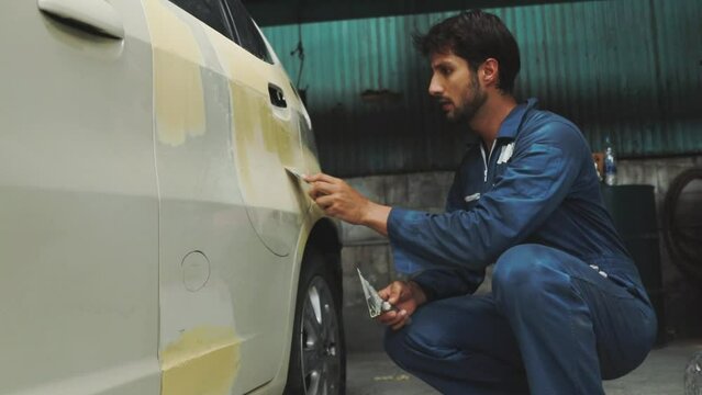 Skilled male car mechanic uses trowel and putty to reinforce smooth, clean surface as a paint job in preparation for smoothing and before repainting : Auto mechanic car accident in modern garage.