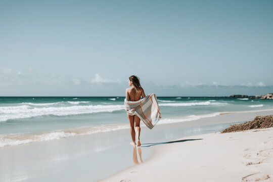 Beachside Stroll: Woman Walking by the Sea with Beach Towel