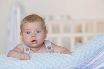 A charming boy in a bright bedroom. A newborn baby is lying on the bed. A child of 4 months looks and smiles at the camera. Bedding for children. Family, pregnancy and childbirth.